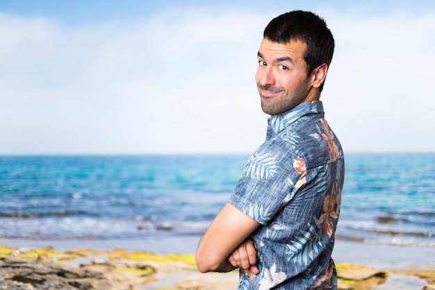 Handsome man with flower shirt with his arms crossed at the beach