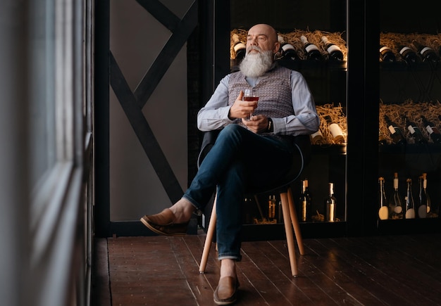 Handsome man with a glass of wine sitting in a chair near a rack of collectible wine