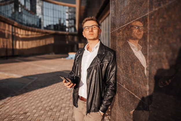 Handsome man with glasses with a smartphone on the street of a big city. Businessman talking on the phone on urban background