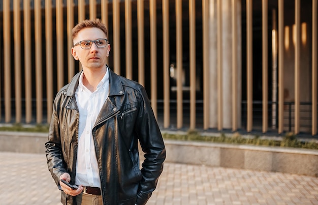 Handsome man with glasses with a smartphone on the street of a big city Businessman talking on the phone on urban background