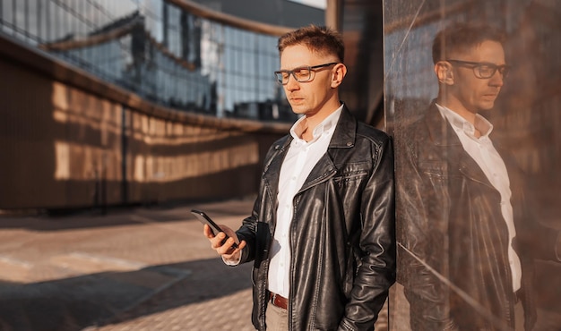 Uomo bello con gli occhiali con uno smartphone sulla strada di una grande città uomo d'affari che parla al telefono sullo sfondo urbano