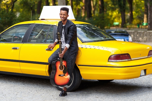 Handsome man with guitar near yellow taxi