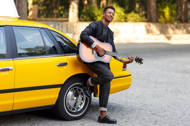 Handsome man with guitar near yellow taxi