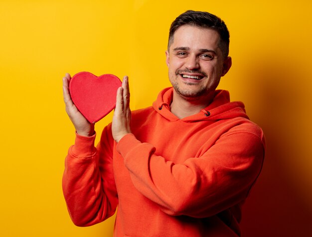 Handsome man with heart shape box on yellow wall