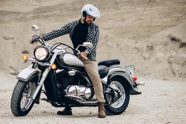 Uomo bello con la sua moto nella cava di sabbia