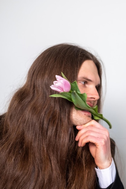 Handsome man with long brown hair holding a tulip in his mouth