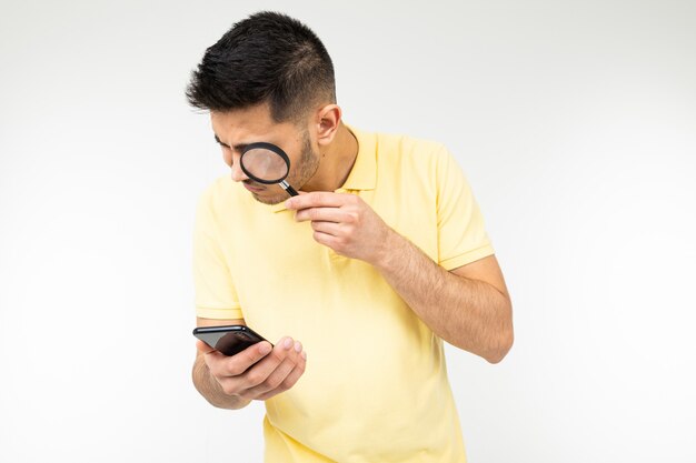 L'uomo bello con ipovisione tiene una lente e uno smartphone in sua mano su un fondo bianco con lo spazio della copia