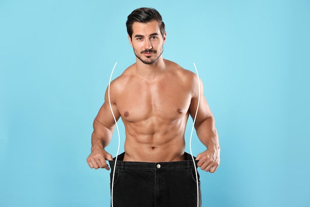 Handsome man with muscular body in oversized jeans on light blue background Weight loss