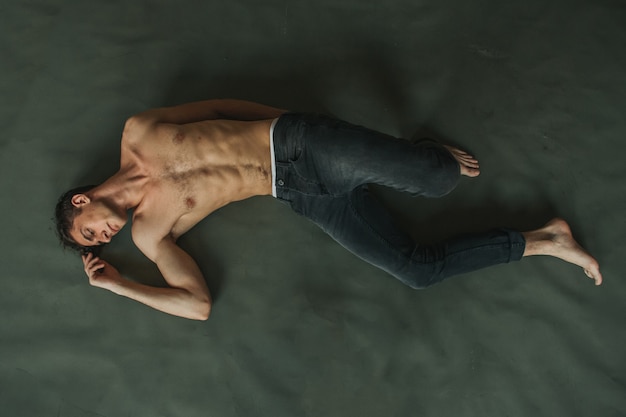 Photo handsome man with naked torso and hairy chest lying on the green floor in jeans.