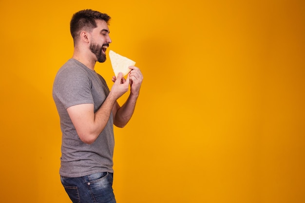 Uomo bello con pezzo di formaggio su sfondo giallo. ragazzo con una fetta di formaggio in mano