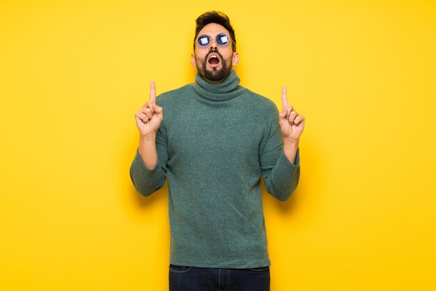 Handsome man with sunglasses surprised and pointing up