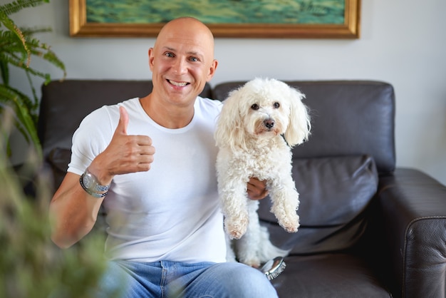 Handsome man with white dog at home on sofa