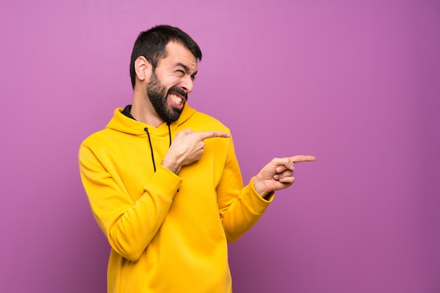 Handsome man with yellow sweatshirt frightened and pointing to the side