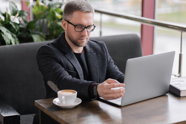 一杯のコーヒーのためにラップトップに取り組んでいるハンサムな男