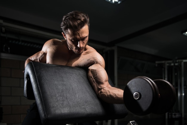 Handsome Man Working Out Biceps In A Dark Gym  Dumbbell Concentration Curls