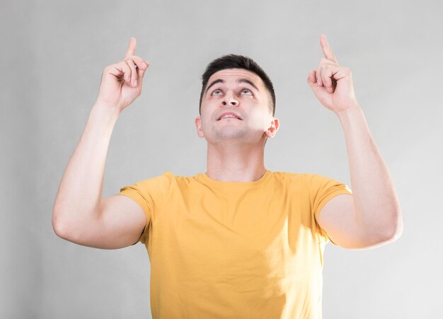 Handsome man in a yellow tshirt pointing finger up isolated on gray background