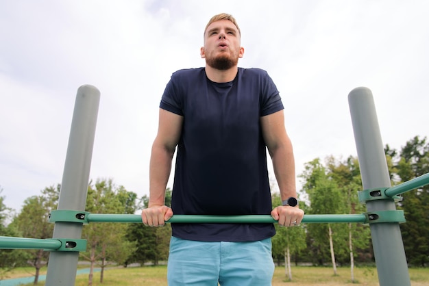 Handsome man young fitness strong athletic guy pulls himself up on horizontal bar outdoors at gym