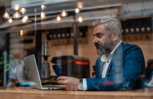 A handsome mature business man using his phone while working on a laptop in the office