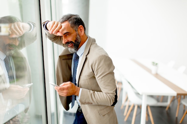 Uomo d'affari maturo bello con il telefono cellulare nell'ufficio