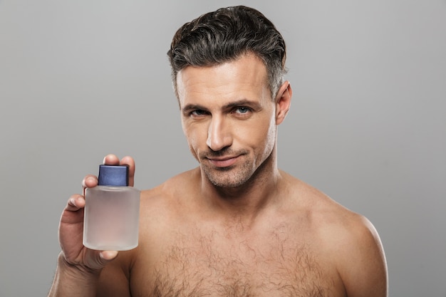 Handsome mature cheerful man holding perfume.