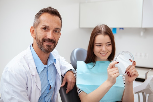 Handsome mature male doctor smiling to the camera, his female patient smiling looking in the mirror