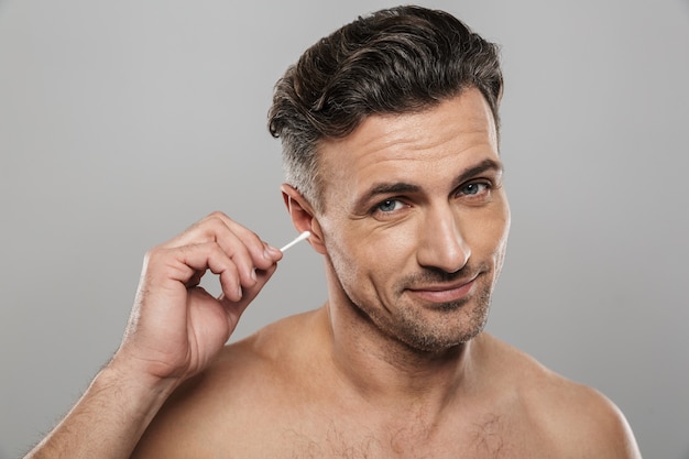 綿棒を持っているハンサムな中年の男性は、耳の掃除をします。