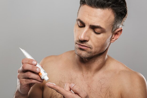 Handsome mature man holding cream. Looking aside.