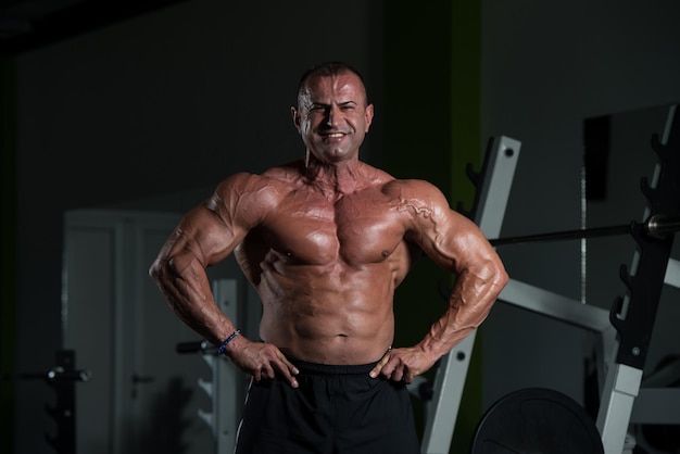 Handsome Mature Man Standing Strong In The Gym And Flexing Muscles  Muscular Athletic Bodybuilder Fitness Male Posing After Exercises