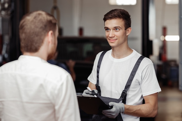 A handsome mechanic is talking to his client about the work done.