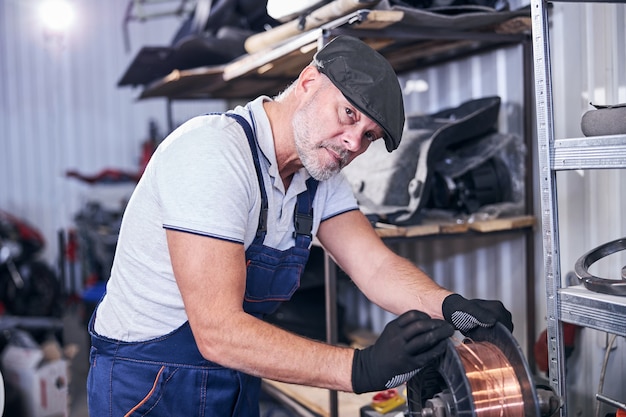 Handsome mechanic using copper wire at vehicle repair shop