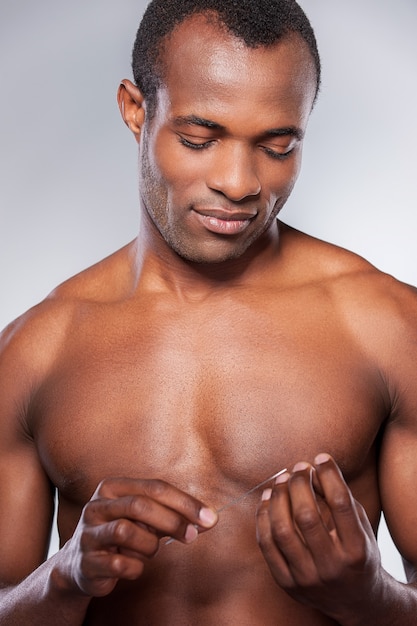 Handsome metrosexual. Young shirtless African man polishing his nails while standing isolated on grey background