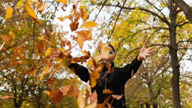 Foto bell'uomo della metà degli anni '30 con gli occhiali verdi nella foresta foglie di alberi decidui gettati via che danno un effetto di magia e assenza di gravità connessione con la natura nella stagione autunnale e invernale