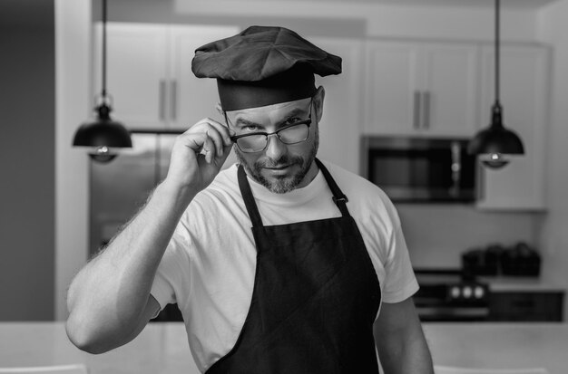 Фото Красивый мужчина средних лет в форме шеф-повара на кухне готовит и кулинарный ресторанный меню концепция