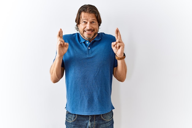 Handsome middle age man standing together over isolated background gesturing finger crossed smiling with hope and eyes closed luck and superstitious concept