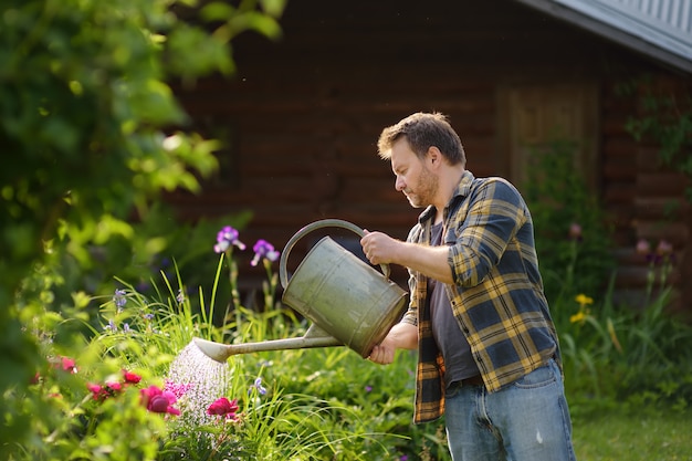 Handsome middle age man watering flowers in the yard in the summer.