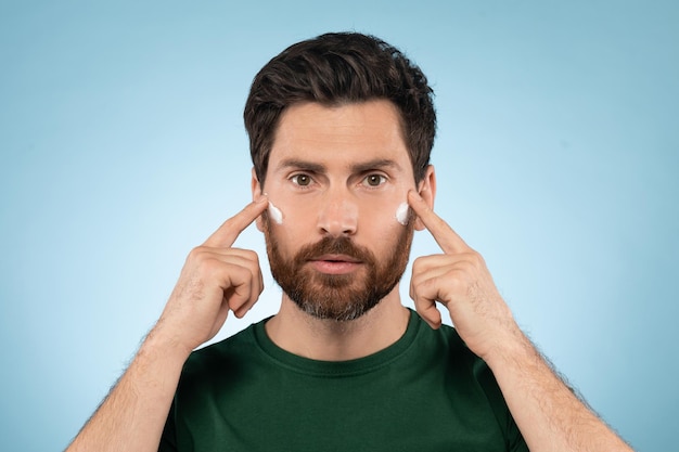 Handsome middle aged man doing regular beauty routine applying face cream on cheeks with fingers