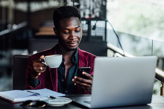 Handsome model, african young man in summer terrace reading news by his phone.