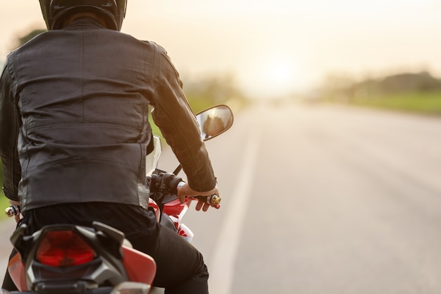 Photo handsome motorcyclist wear leather jacket, holding helmet on the road