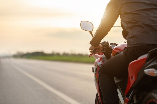 ハンサムなモーターサイクリストは道路でバイクの上に座って革のジャケットを着る