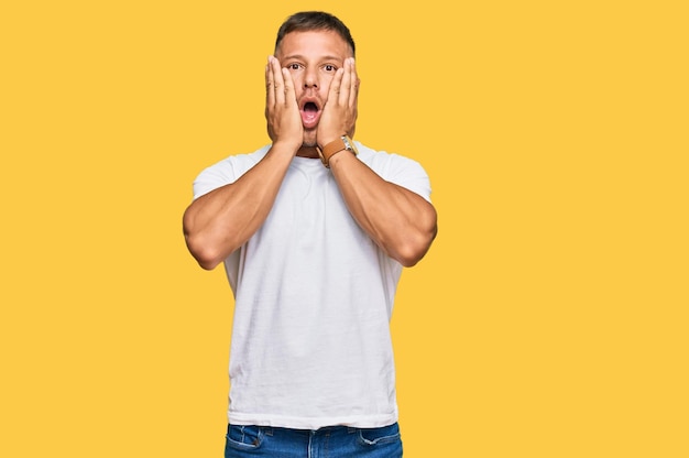 Handsome muscle man wearing casual white tshirt afraid and shocked, surprise and amazed expression with hands on face