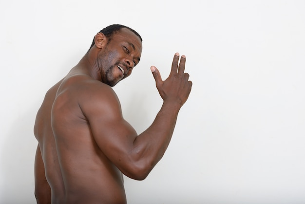 handsome muscular bearded African man shirtless against white wall