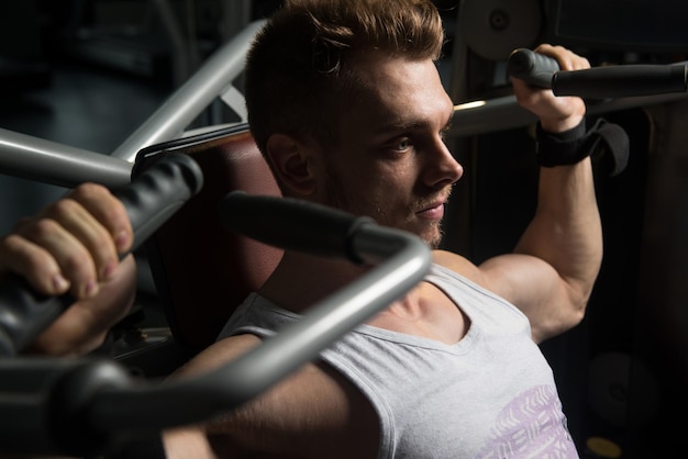 Handsome Muscular Fitness Bodybuilder Doing Heavy Weight Exercise For Shoulders On Machine In The Gym