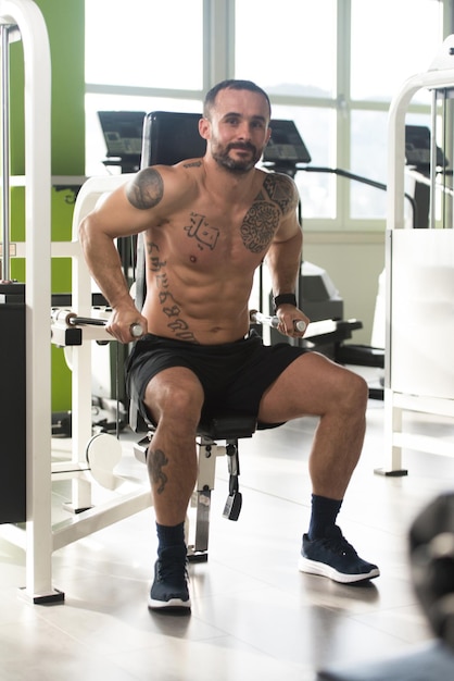 Handsome Muscular Fitness Bodybuilder Doing Heavy Weight Exercise For Triceps On Machine In The Gym