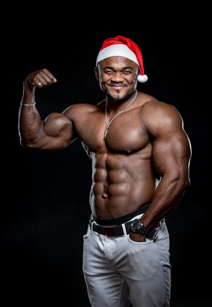 Handsome muscular man in christmas hat showing his biceps. Athletic fitness santa claus with naked torso.