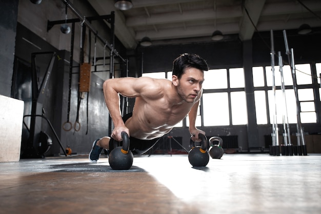 Handsome muscular man doing pushup exercise with dumbbell in a crossfit workout.