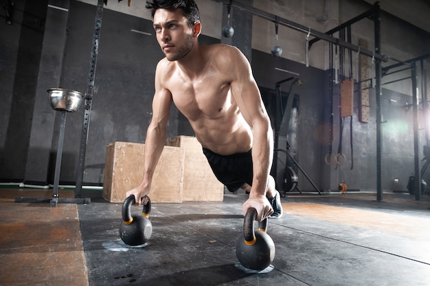 Handsome muscular man doing pushup exercise with dumbbell in a crossfit workout.