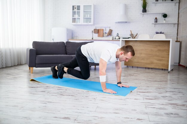 Handsome muscular man in a t-shirt is doing functional exercises on the floor at home. Fitness at home. Healthy lifestyle.