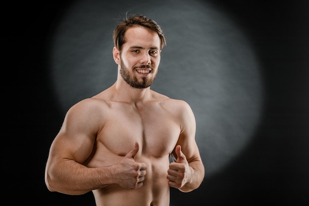 A handsome muscular man without a tshirt poses for a photographer in a dark photo Studio The concept of sport