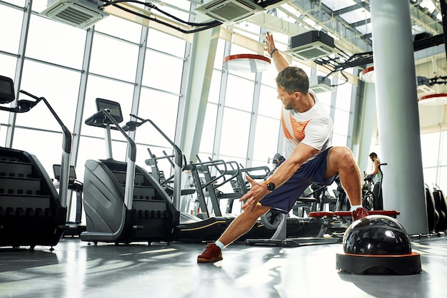 잘생긴 근육질의 남자는 체육관 배경에서 기능 훈련 소프트 플랫폼에서 운동합니다