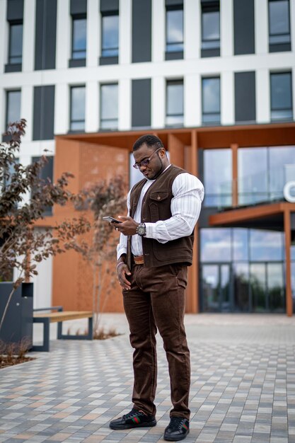 Handsome office manager looking on mobile phone outdoor and smiling. Looking confident and having important conversation. Serious man wearing stylish formal clothes